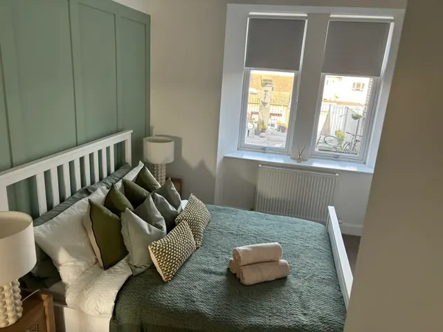 Double bedroom with sage panelled wall, white bed frame and cosy green cushions